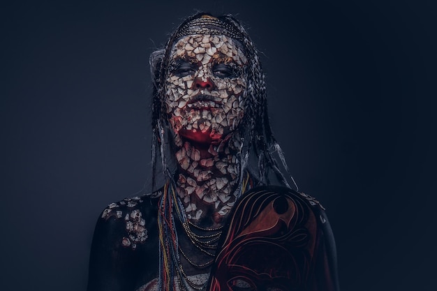Portrait of a scary African shaman female with a petrified cracked skin and dreadlocks on a dark background. Make-up concept.