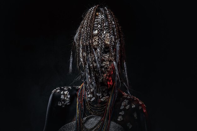 Portrait of a scary African shaman female with a petrified cracked skin and dreadlocks on a dark background. Make-up concept.