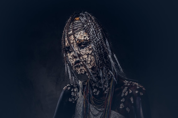 Portrait of a scary African shaman female with a petrified cracked skin and dreadlocks on a dark background. Make-up concept.