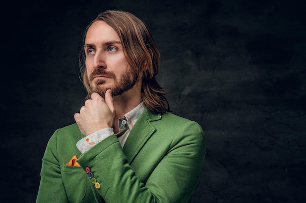Портрет скептически настроенного творческого человека в зеленом блейзере на темном фоне.