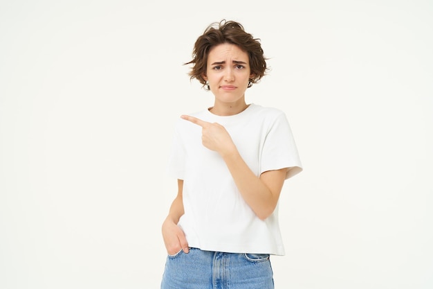 Free photo portrait of sceptical young woman pointing finger left and looking with doubt at camera dislike smth