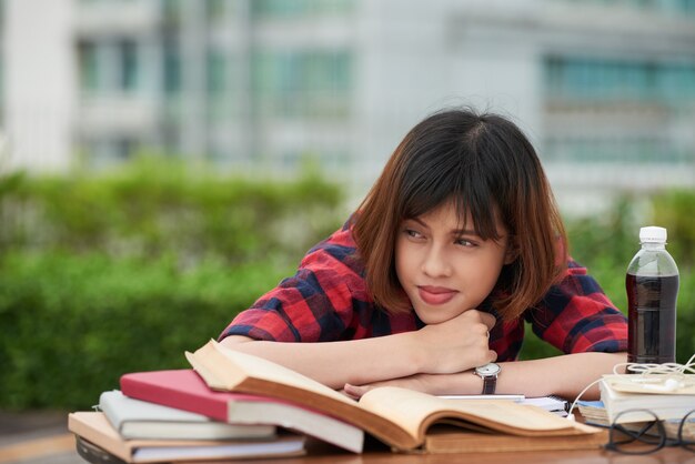 Portrait of schoolgirl tired of hometask routine resting on table cluttered with textbooks