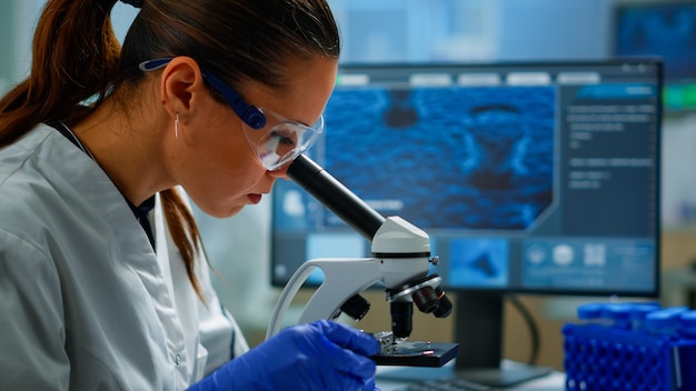 医療開発研究所で顕微鏡下を見て、ペトリ皿のサンプルを分析している科学者の肖像画。医学、先端製薬研究所でのバイオテクノロジー研究、ウイルスの進化の調査