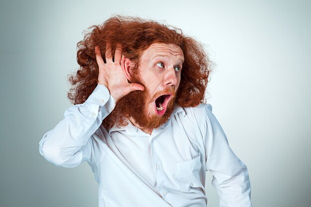 Portrait of screaming young man with long red hair and shocked facial expression on gray background