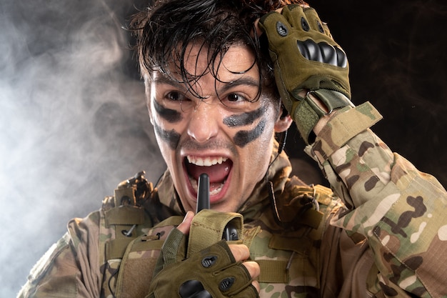Portrait of screaming young soldier in camouflage on dark wall