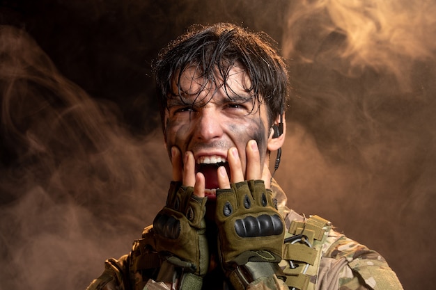 Портрет кричащего молодого солдата в форме на темной стене