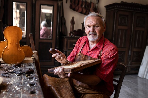 彼の昔ながらのワークショップでツールと木材を保持しているシニア大工の肖像画