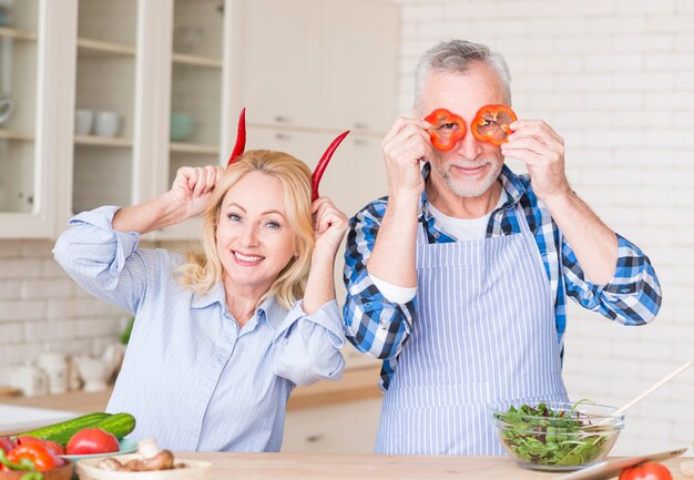赤唐辛子とピーマンの台所でカメラ目線を保持している年配のカップルの肖像画