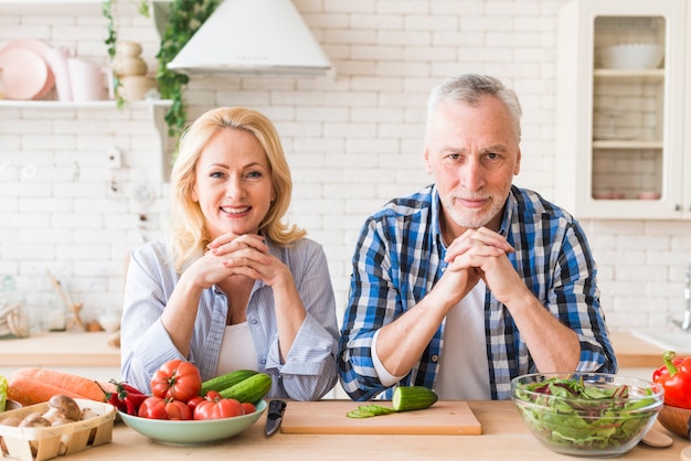 Portrait of a senior couple leaning on wooden table looking at camera