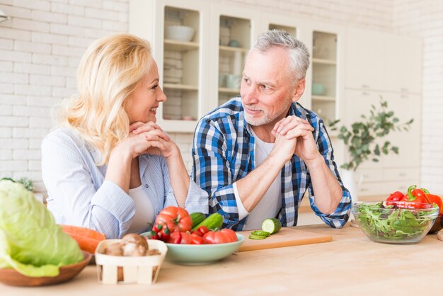 Portrait of a senior couple leaning on wooden table looking at each other in the kitchen
