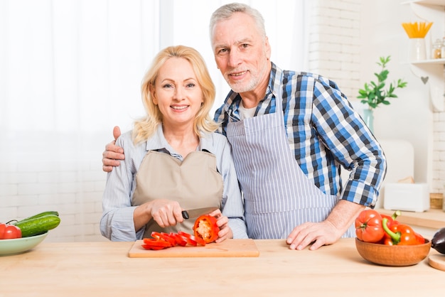 Portrait of a senior couple looking at camera preparing the vegetable