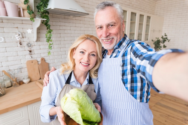 Portrait of a senior couple taking selfie on mobile phone in the kitchen