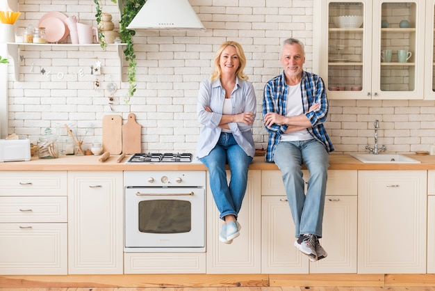 Портрет пожилой пары со скрещенными руками сидит на кухонном столе