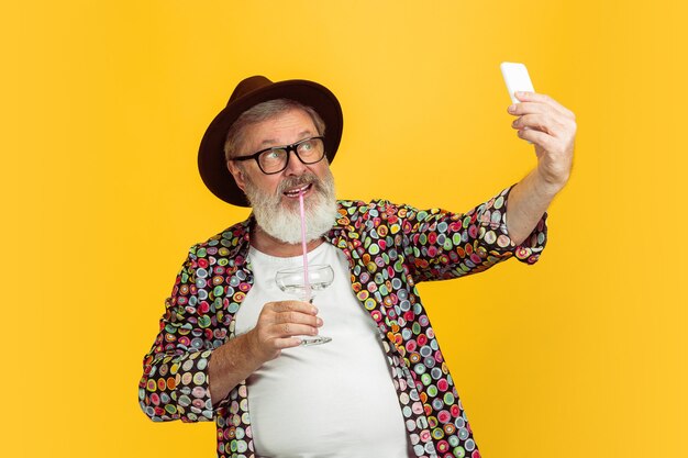 장치, 노란색 스튜디오 배경에 고립 된 가제트를 사용 하여 수석 hipster 남자의 초상화. 기술과 즐거운 노인 라이프 스타일 개념.
