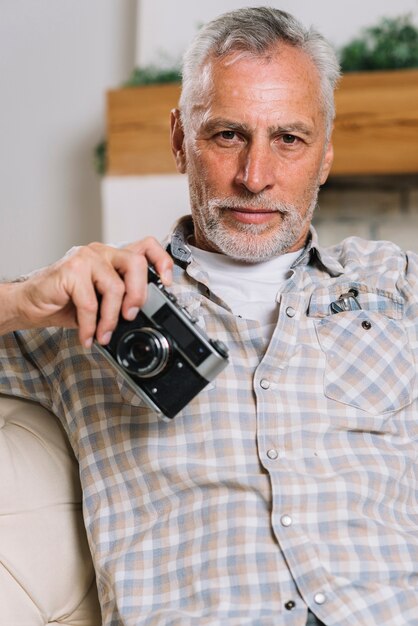 Portrait of senior man holding camera in hand looking at camera