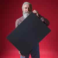 Foto gratuita ritratto di un uomo anziano che mostra cartello nero bianco in piedi contro il contesto rosso