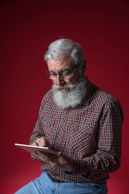 赤い背景に対してデジタルタブレットを使用して年配の男性の肖像画