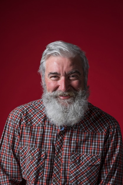 Portrait of a senior man with grey beard looking to camera against red backdrop