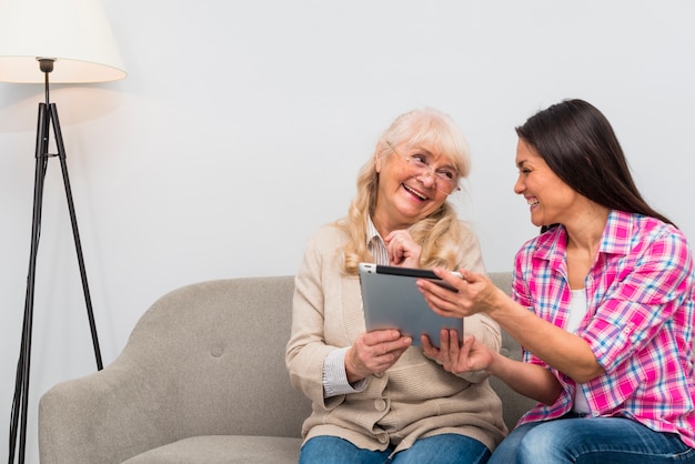 Portrait of senior mother and young daughter holding digital tablet in hand looking at each other