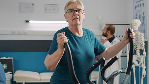 Портрет пожилой женщины, занимающейся физиотерапией на велотренажере, использующей электрический велосипед для лечения механических заболеваний. Пожилой пациент делает реабилитационные упражнения для повышения подвижности.