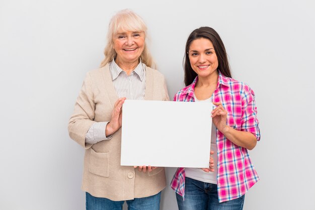 Portrait of senior woman and her daughter showing blank white placard