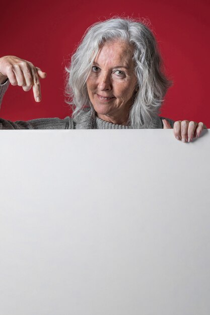 白い空白のプラカードを下向きに彼女の指を指している年配の女性の肖像画