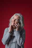 Free photo portrait of a senior woman talking on mobile phone looking up against red background