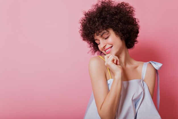 Portrait of sensitive short-haired with ringlets woman dressed sky blue blouse poses with charming smile on pink