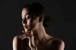 Foto gratuita ritratto di bella donna sensuale che osserva da parte mentre si tocca il mento in condizioni di scarsa luminosità, isolato sopra il nero