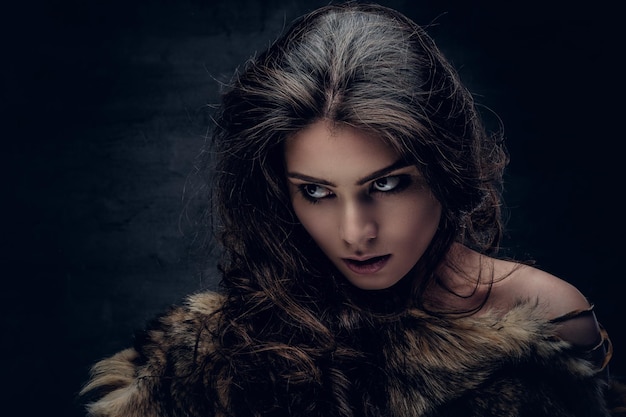 깊은 그림자에 회색 배경에 따뜻한 모피 코트를 입은 관능적 인 갈색 머리 여성의 초상화.