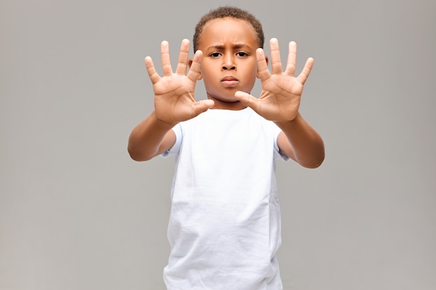 심각한 아프리카 계 미국인 소년의 초상화는 흰색 티셔츠를 입고 심술 궂은 표정을 짓고 두 손에 10 개의 손가락을 모두 보여주는 제스처 또는 정지 신호를 표시하지 않습니다.