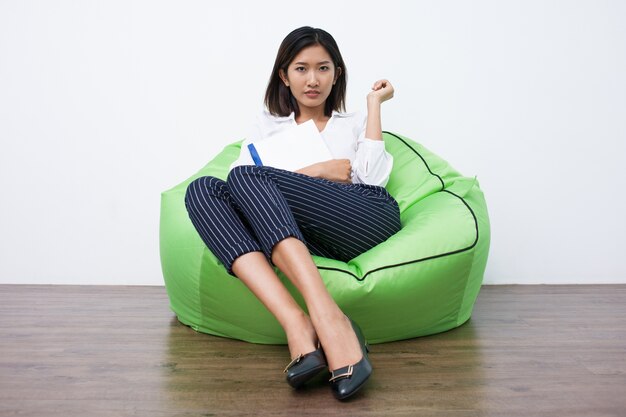 Portrait of serious Asian businesswoman sitting on beanbag