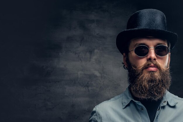 Портрет серьезного бородатого мужчины в солнцезащитных очках и цилиндрической шляпе.