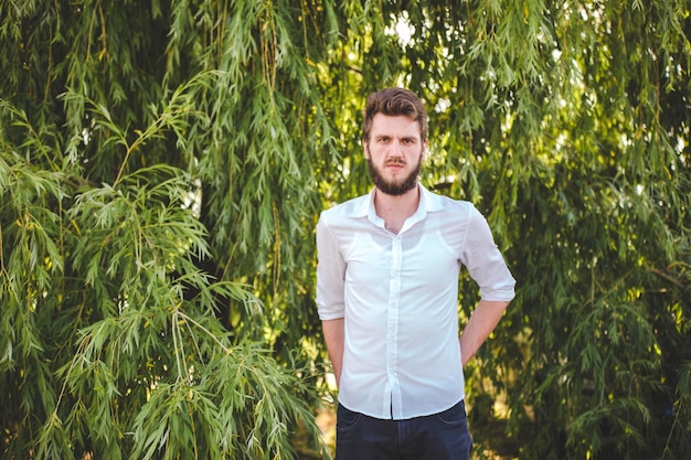 Portrait of a serious caucasian man in a shirt against green trees