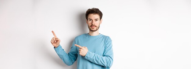 Portrait of serious caucasian man with beard pointing right at logo and looking at camera standing i