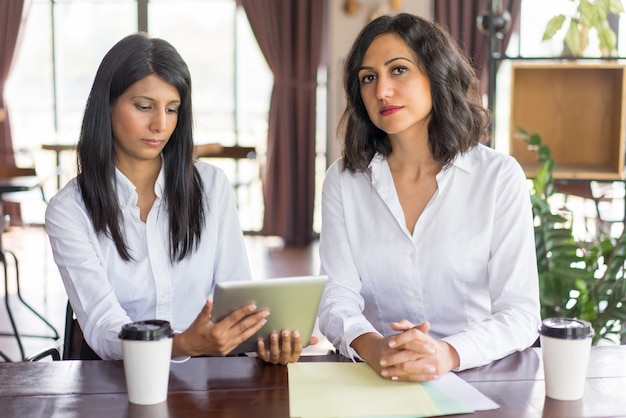 Portrait of serious female executive and her secretary with digital tablet. 