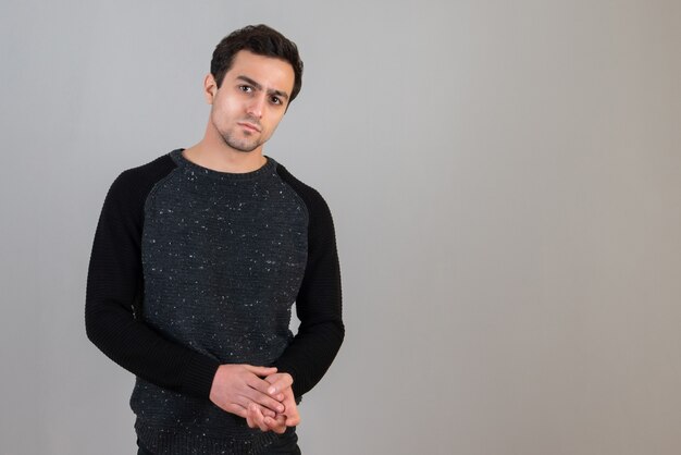 Portrait of serious handsome man in black sweater posing on gray wall