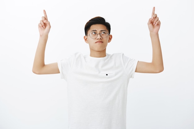 Portrait of serious-looking charming young chinese male student in white t-shirt raising hands