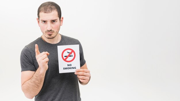 Portrait of a serious man holding no smoking sign pointing finger toward camera