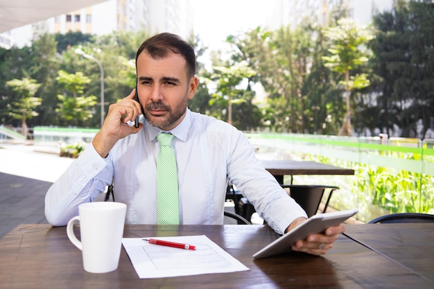 Portrait of serious manager sitting at cafe and calling partner