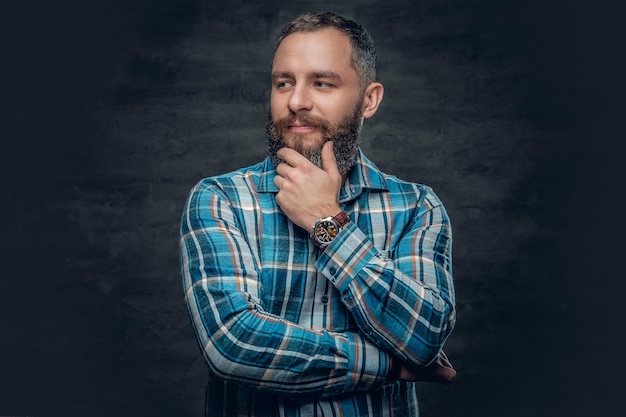 Ritratto di un uomo barbuto di mezza età serio vestito con una camicia di flanella a quadri su sfondo grigio.