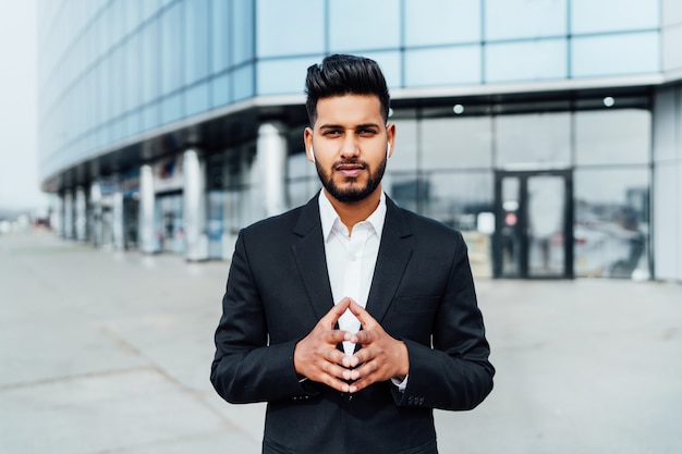 Portrait of a serious smiling modern Indian man near a office building