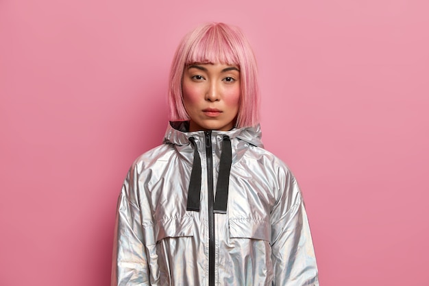 Free photo portrait of serious woman with stylish pink hairstyle, perfect fresh clean skin, looks with calm confident expression, dressed in silver jacket