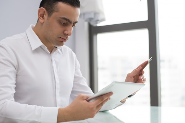 Free photo portrait of serious young businessman working on digital tablet