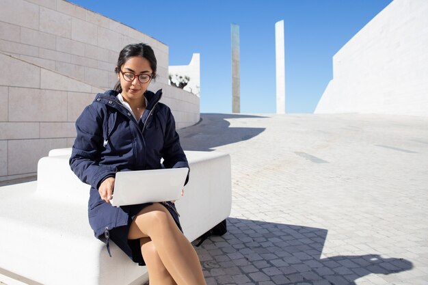 Portrait of serious young freelancer working on laptop outdoors