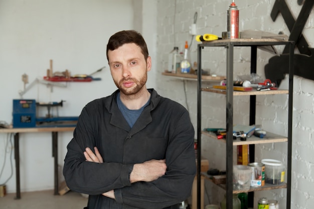 Portrait of serious young handyman standing in own workshop interior