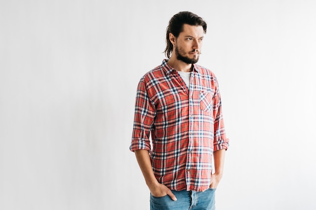 Portrait of a serious young man with hands in his pocket looking away against white background