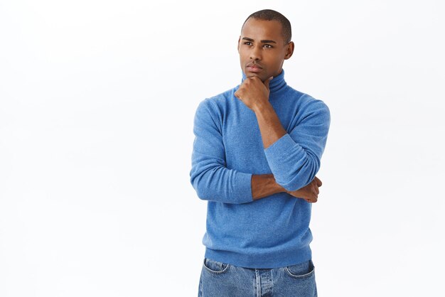 Portrait of seriouslooking young smart african american man in blue turtleneck frowning look at chart or something important with pondering focused face touch chin thoughtful