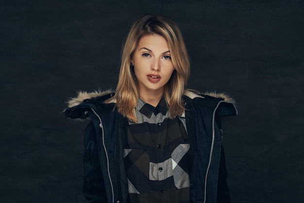 Free photo portrait of a sexy blonde girl in a winter jacket and fleece shirt, standing in a studio. isolated on a dark background.