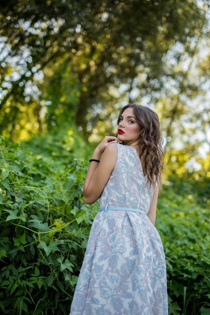 Portrait of a sexy brunette girl in nature looking back over her shoulder in a light summer dress